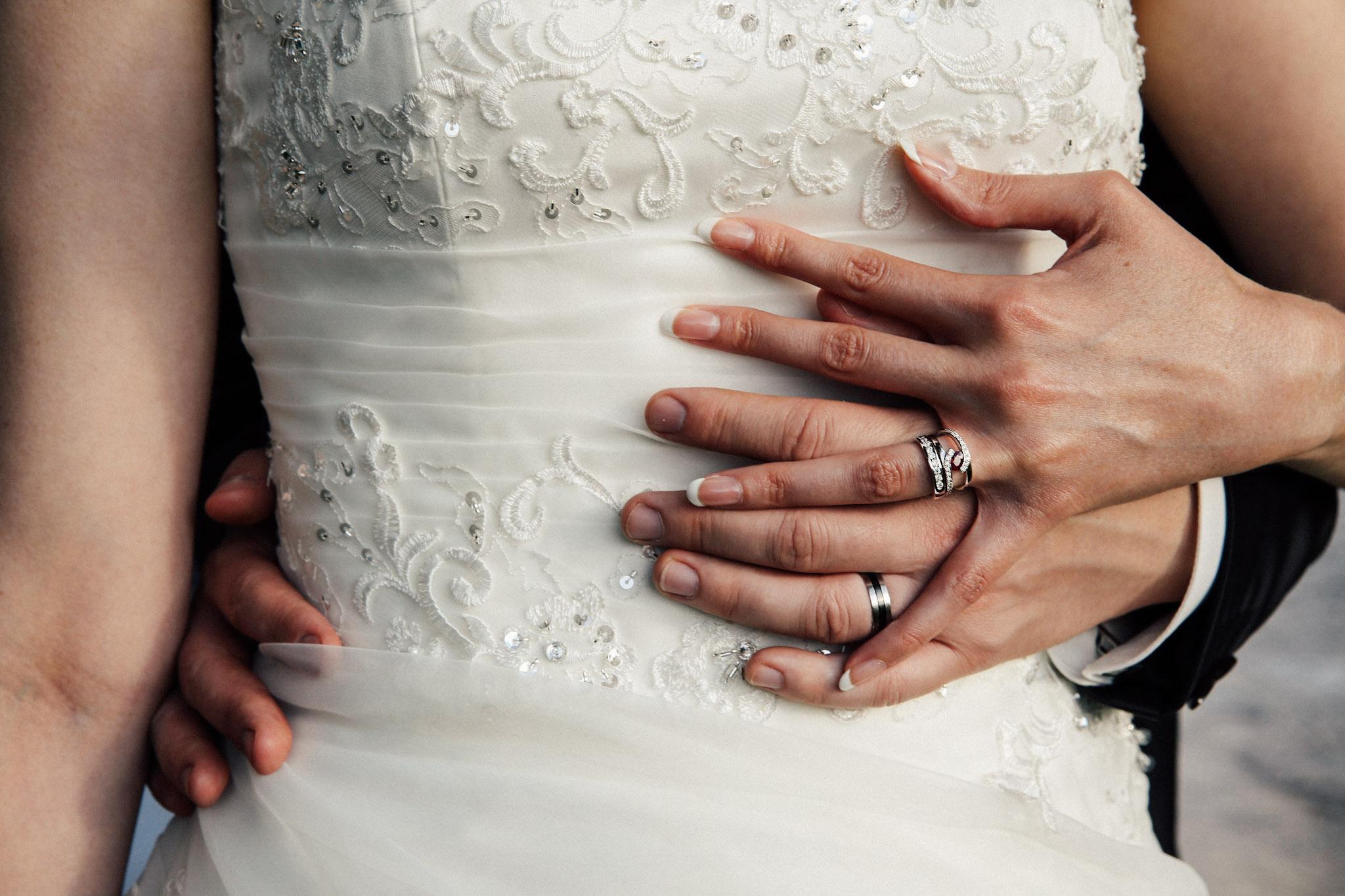 Couple de jeunes mariés en closeup se tenant la main, avec vue sur les alliances